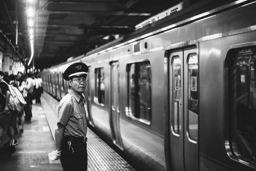 man in officer hat standing in front of train