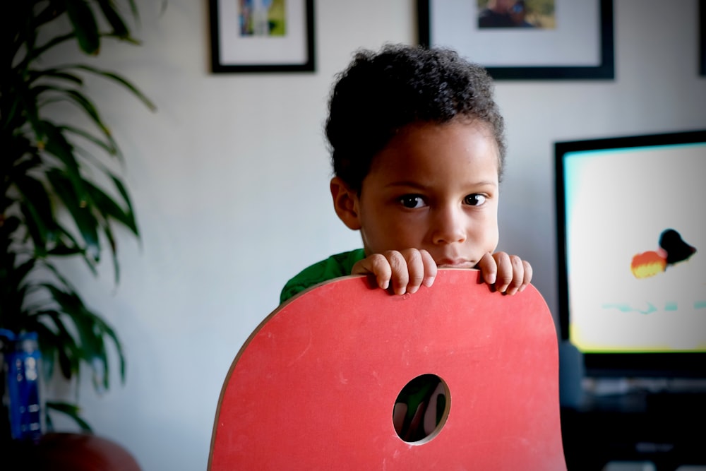 boy holding red chair near black flat screen TV