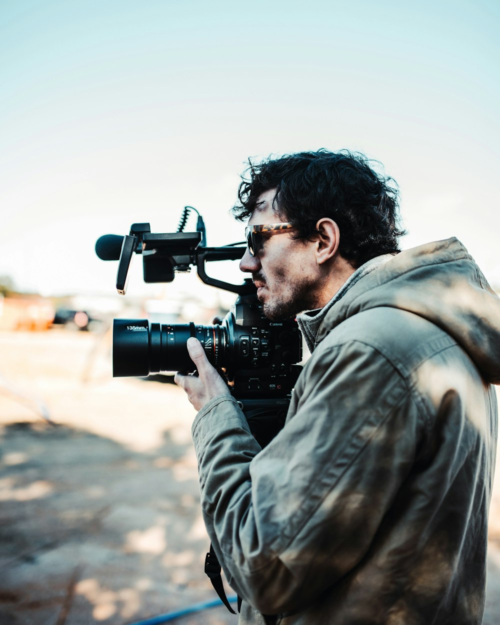 man in brown coat holding video camera on selective focus photography