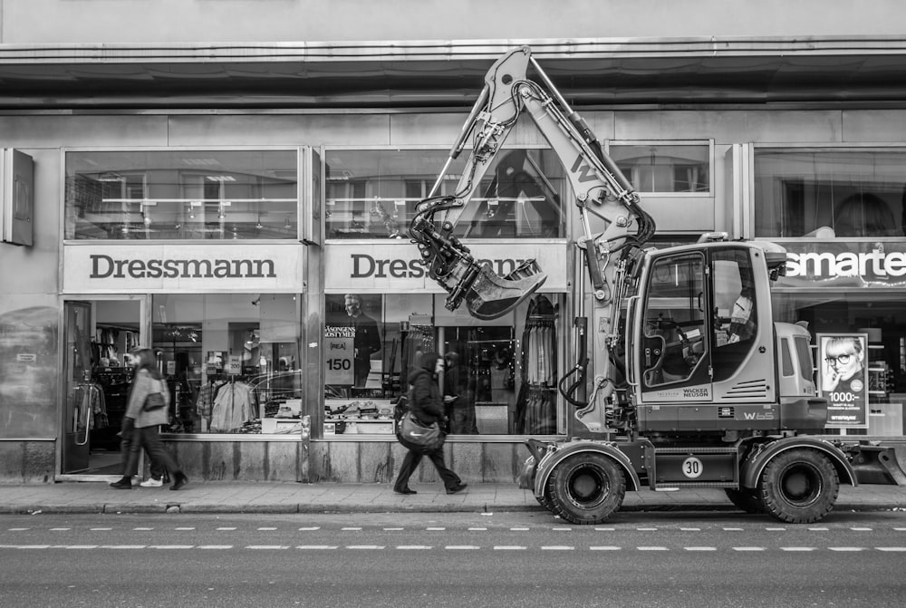 greyscale photo of excavator beside building