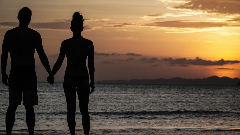 silhouette photography of man and woman holding hands front of the sea