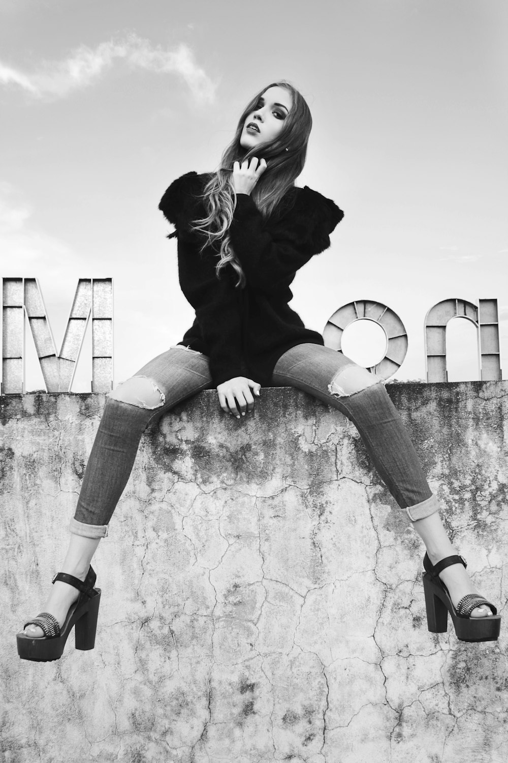 grayscale photography of woman sitting on wall