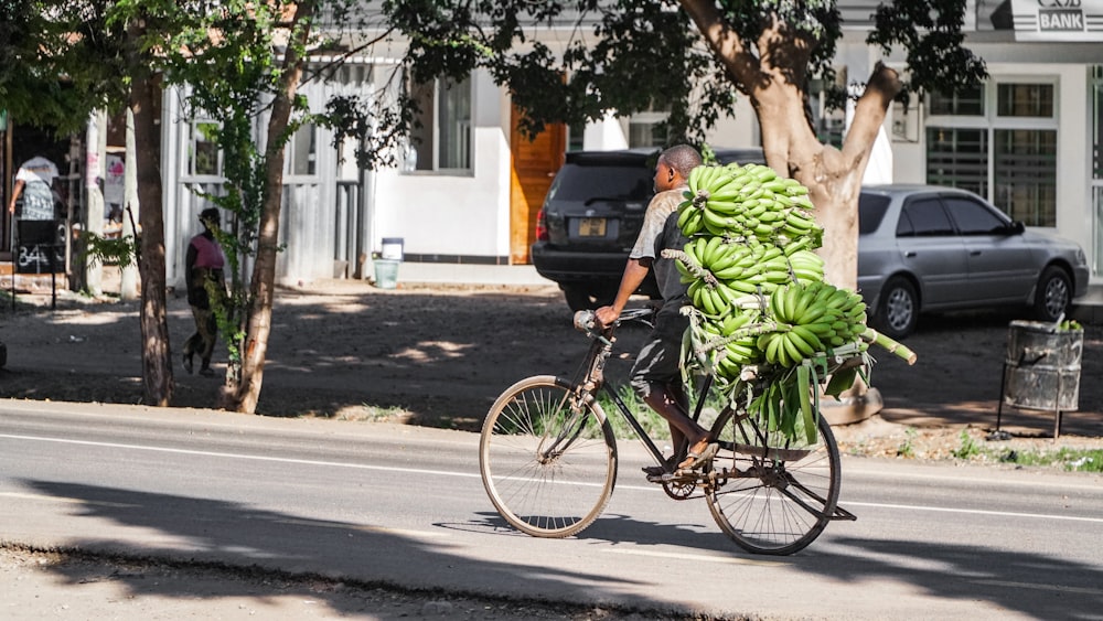 man riding bicycle while carrying bunch of bananas