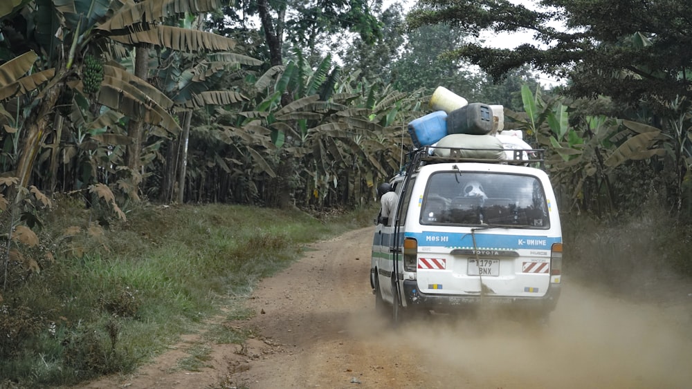 assorted-color plastic containers on top of white van travelling on brown dirt road near green banana trees during daytime