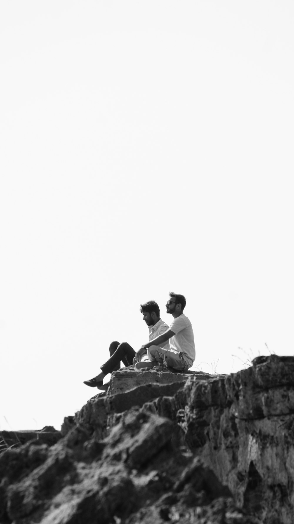 two men sitting on cliff in black and white photography