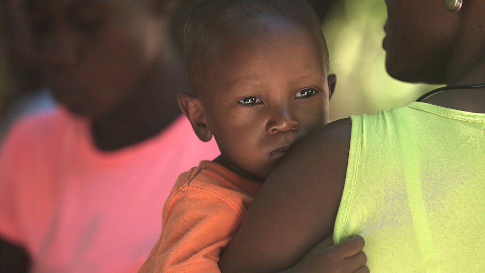 woman carries boy in orange shirt