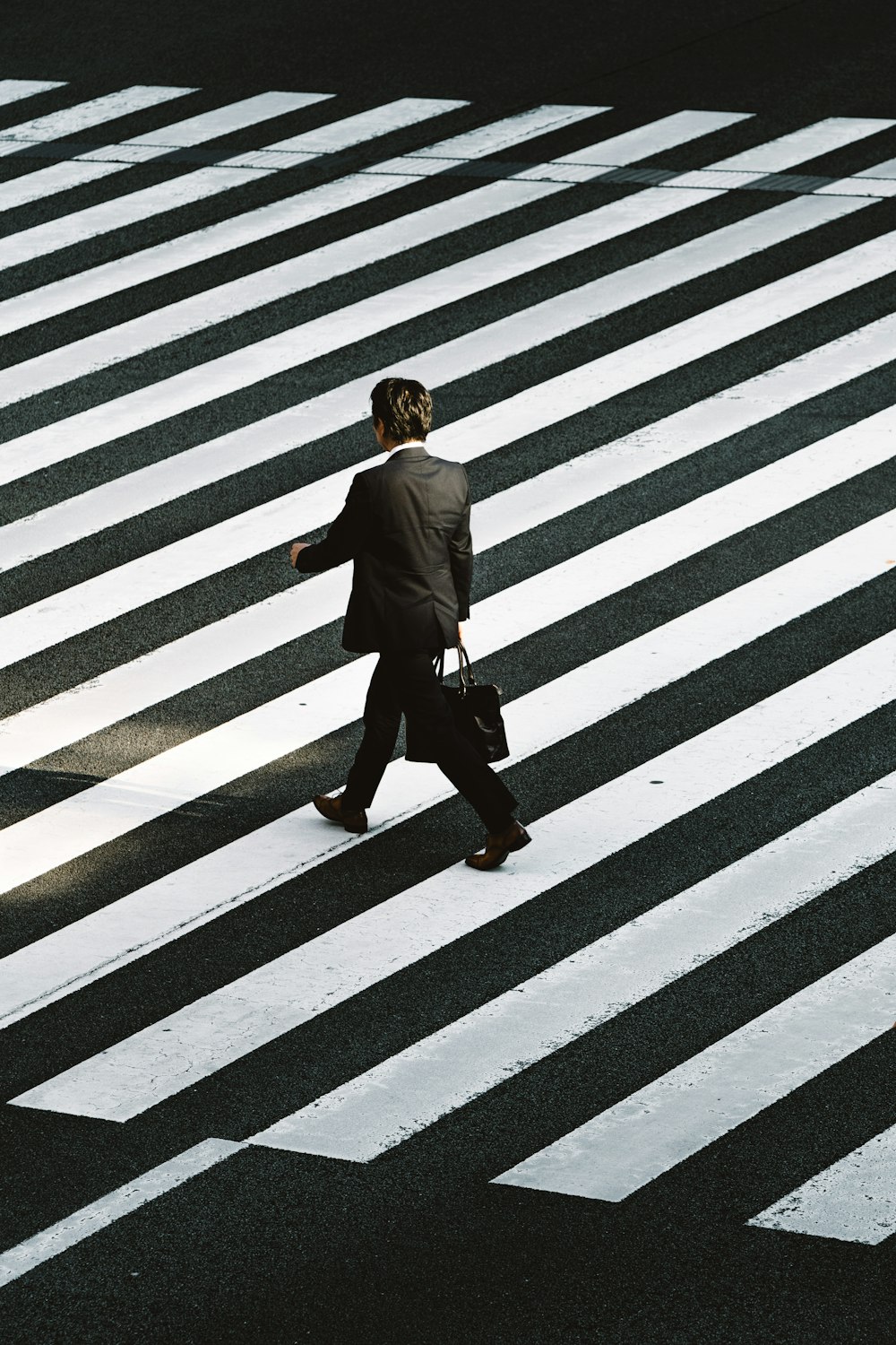 man in black formal suit jacket and pants carrying black bag while walking on pedestrian lane during daytime