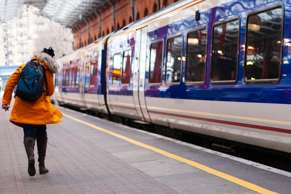 woman in orange coat walking beside train at the station