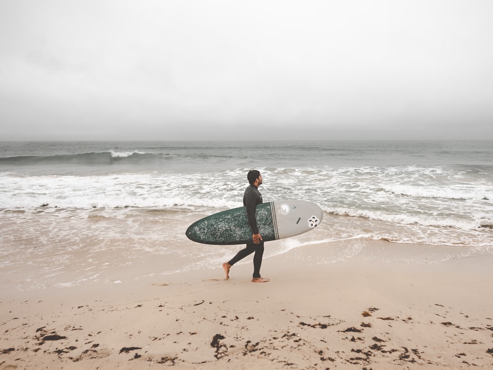 uomo che tiene la tavola da surf in riva al mare durante il giorno