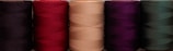 A row of colorful spools of thread in maroon, indigo, and gold hues ready for weaving.