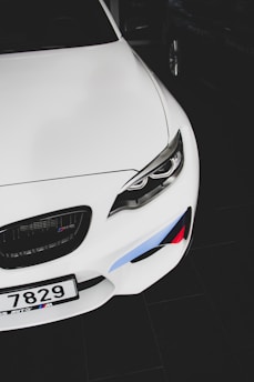 A white sports car featuring sleek lines and a prominent front grille. The design includes sharp, modern headlights and distinctive colored accents on the bumper, adding a touch of sporty flair. The license plate is also visible, contributing to the car's identity.