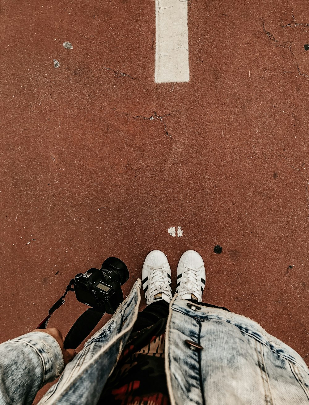 person wearing white adidas Superstar holding DSLR camera