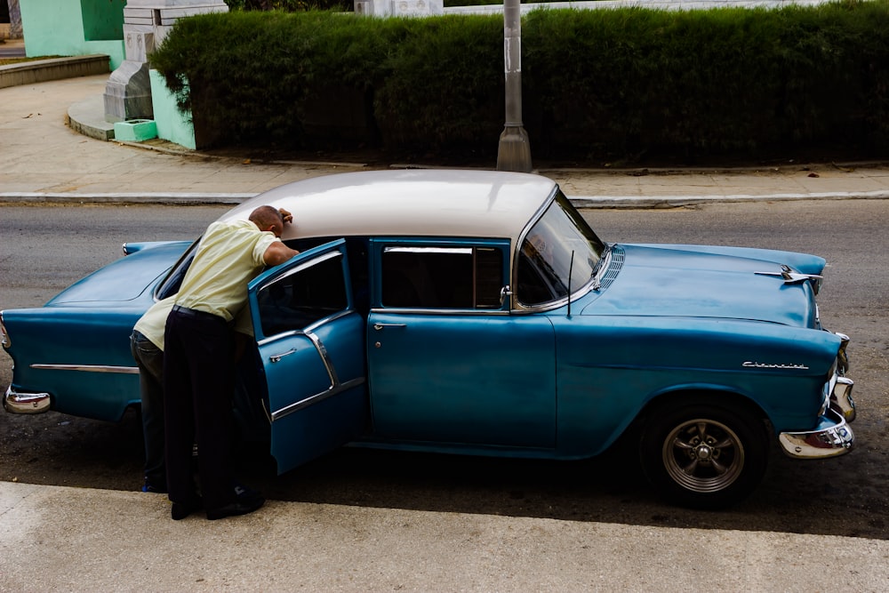 man standing in front of blue sedan during daytime