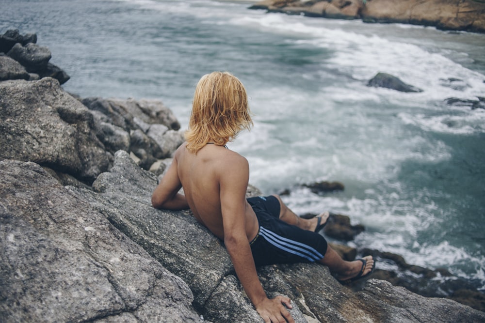 man sitting on rock formation beside sea during daytime