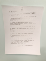 A piece of white paper is pinned to a light blue wall with a clear thumbtack. The paper contains a list of typed quotes, numbered from 1 to 13, each with a unique philosophical or motivational message.