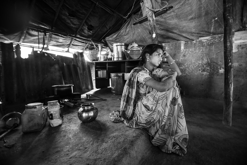 grayscale photography of woman siting leaning on wooden post