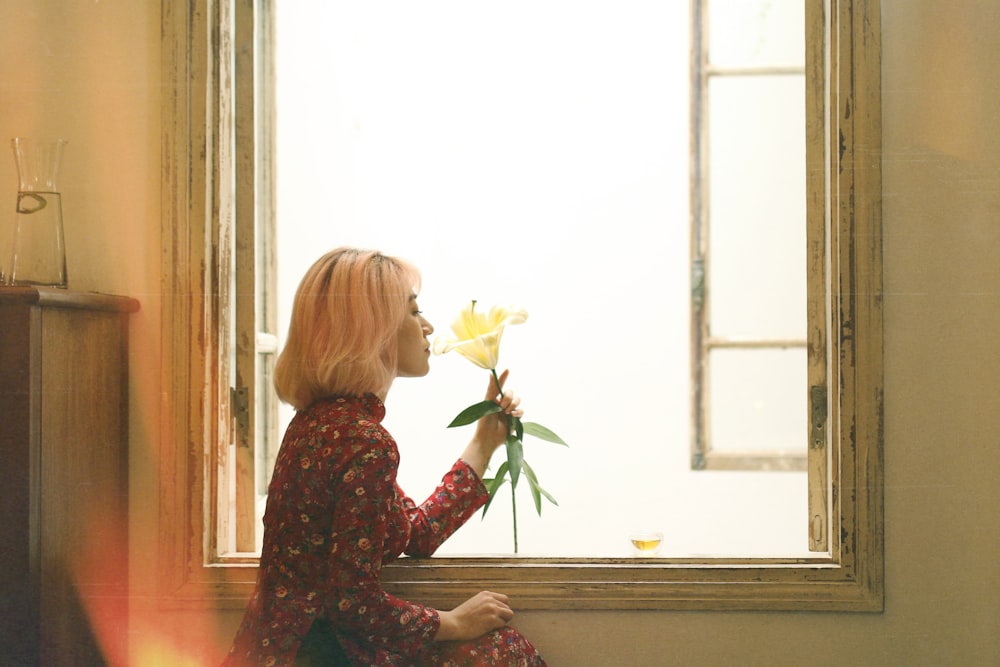 mulher cheirando flor branca ao lado da janela