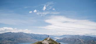 A scenic view of a traveler standing on a mountain peak overlooking a valley.
