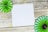 A wooden surface with a white square piece of paper in the center. Green and dark green paper pinwheels are positioned at opposite corners, adding a decorative element.