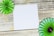 A wooden surface with a white square piece of paper in the center. Green and dark green paper pinwheels are positioned at opposite corners, adding a decorative element.