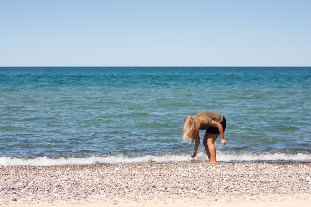 a woman bending over on a beach next to the ocean