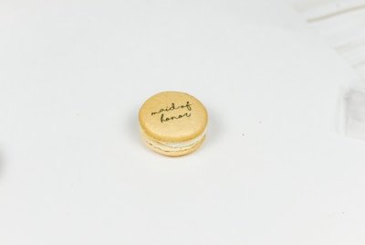 A single macaron on a light, plain background with 'maid of honor' written on top in cursive.