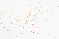 Small, vibrant fruit-shaped confetti scattered across a white background.