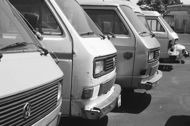 A row of light commercial vans lined up, showcasing various stages of mechanical and bodywork restoration.