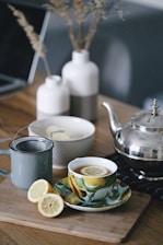 gray teapot beside mug filled with tea and lemon on top of table