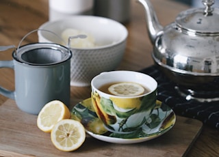 gray teapot beside mug filled with tea and lemon on top of table