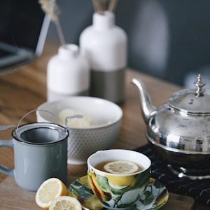 gray teapot beside mug filled with tea and lemon on top of table