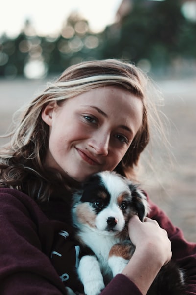A smiling woman holding a small Australian Shepherd puppy close to her chest