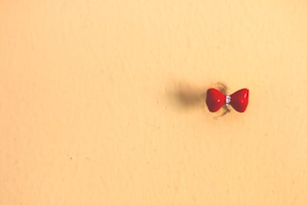 A small red bow with a gem at the center is pinned to a light beige background wall.