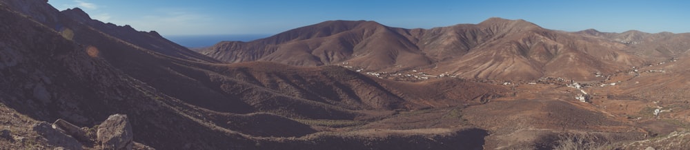 brown open field mountain range under blue sky