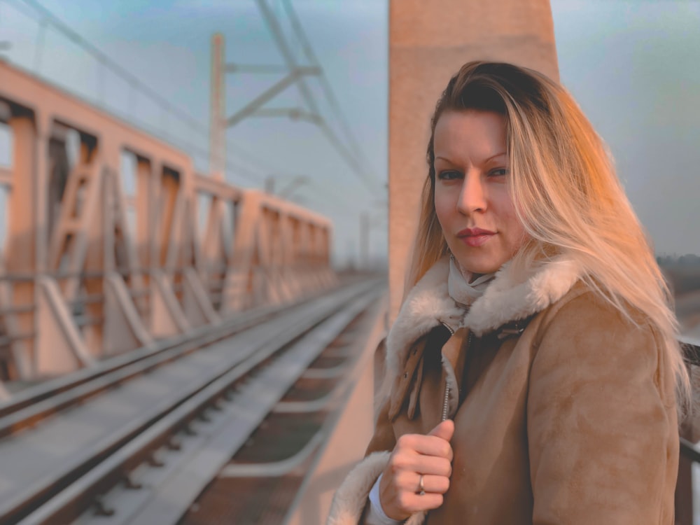 woman wearing brown jacket standing near train rails