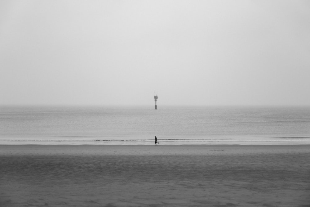 Foto en escala de grises de una persona corriendo en la orilla del mar
