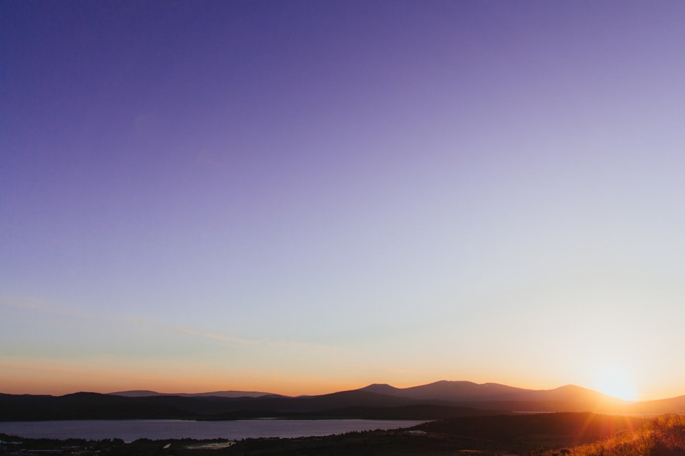 Silueta de montañas cerca del cuerpo de agua durante la puesta del sol naranja