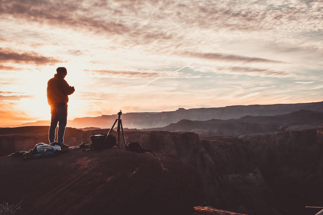 silhouette of person standing on mountain with tripod camera during sunset