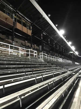 Close-up of a Celina Bobcats hat resting on a wooden bleacher with stadium lights glowing in the background.