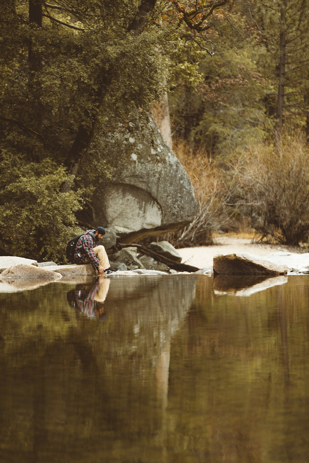 man sitting near lake surrounded with trees