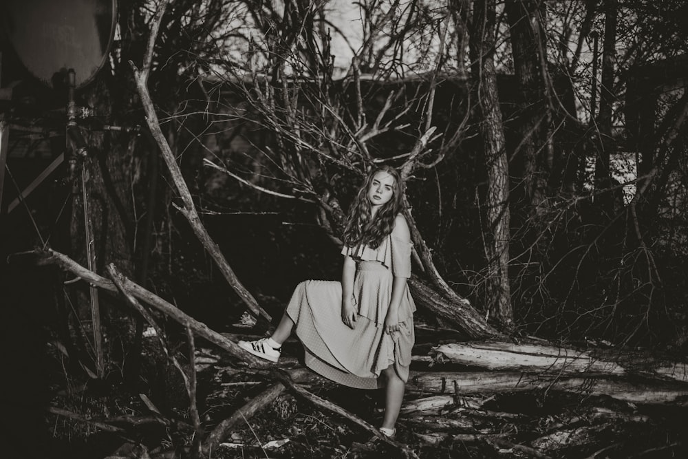 grayscale photo of woman in dress standing on tree branch