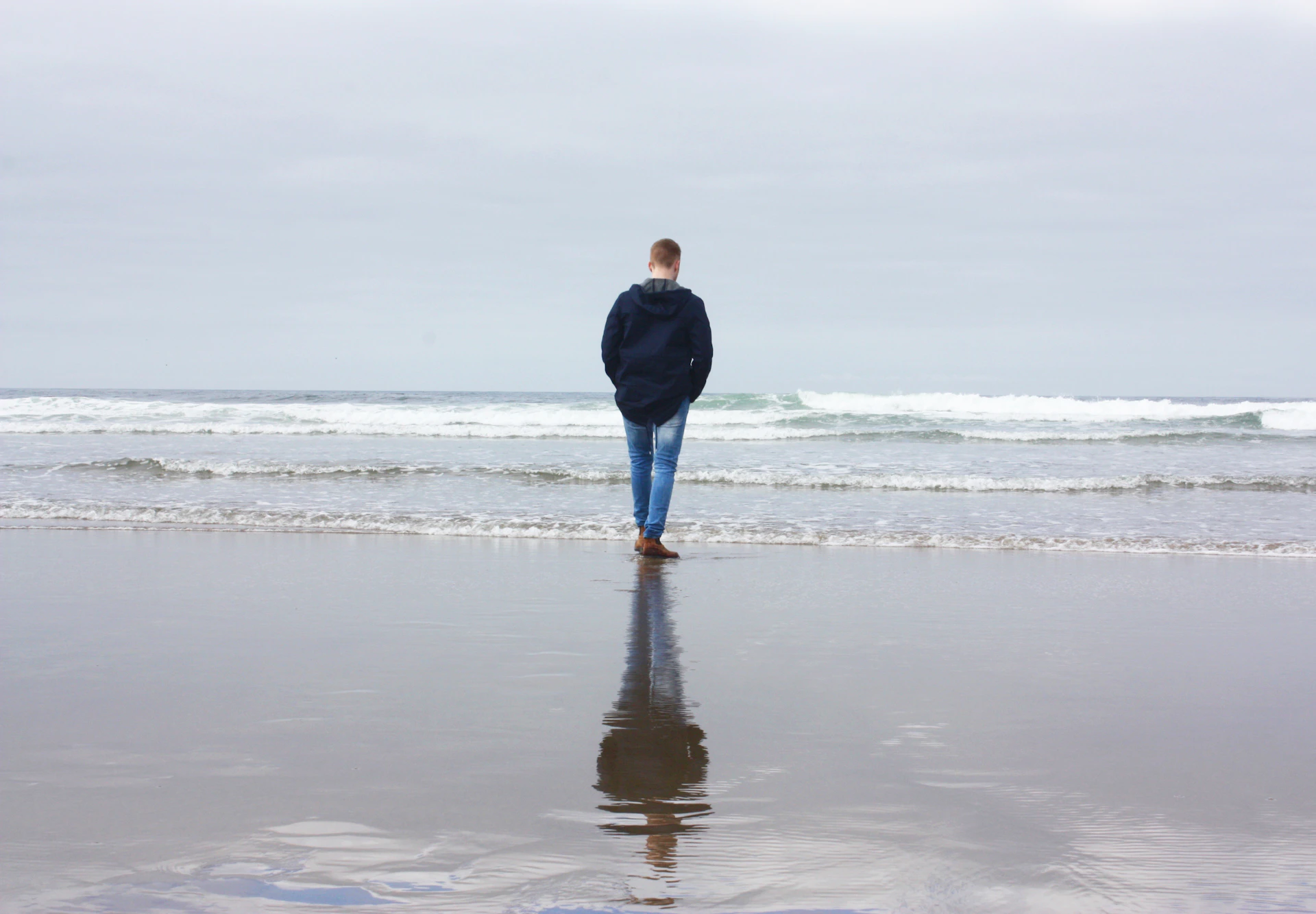 men's blue jacket standing beside body of water during daytime