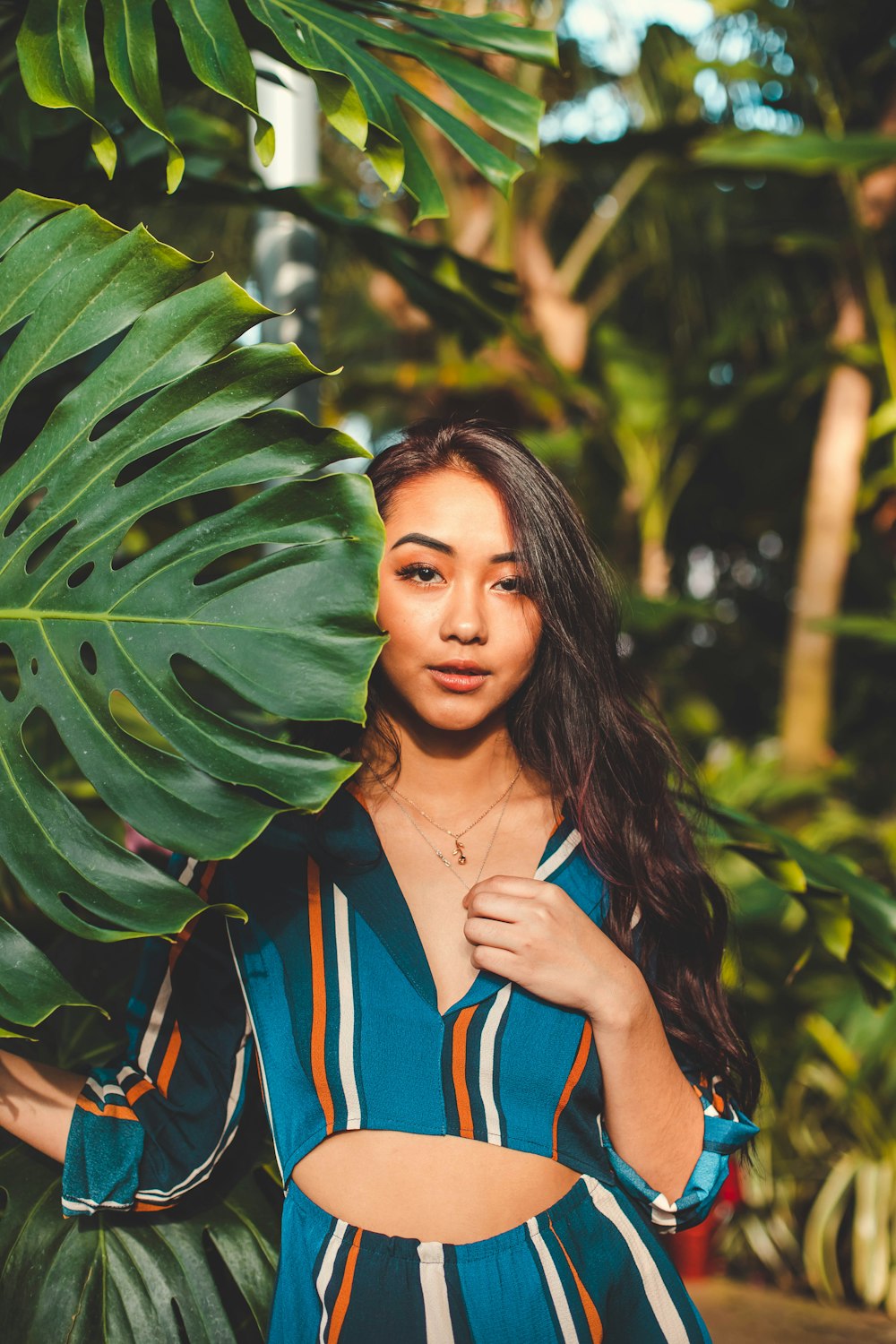 woman in blue and orange striped dress behind large green leaf