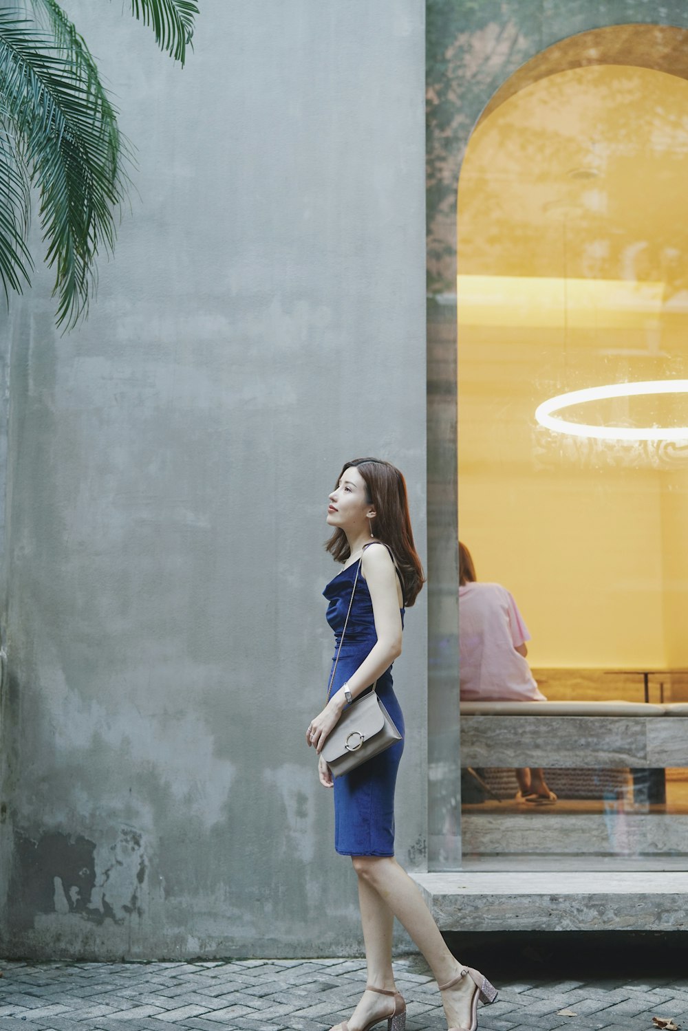 woman in blue dress walking with grey leather sling bag