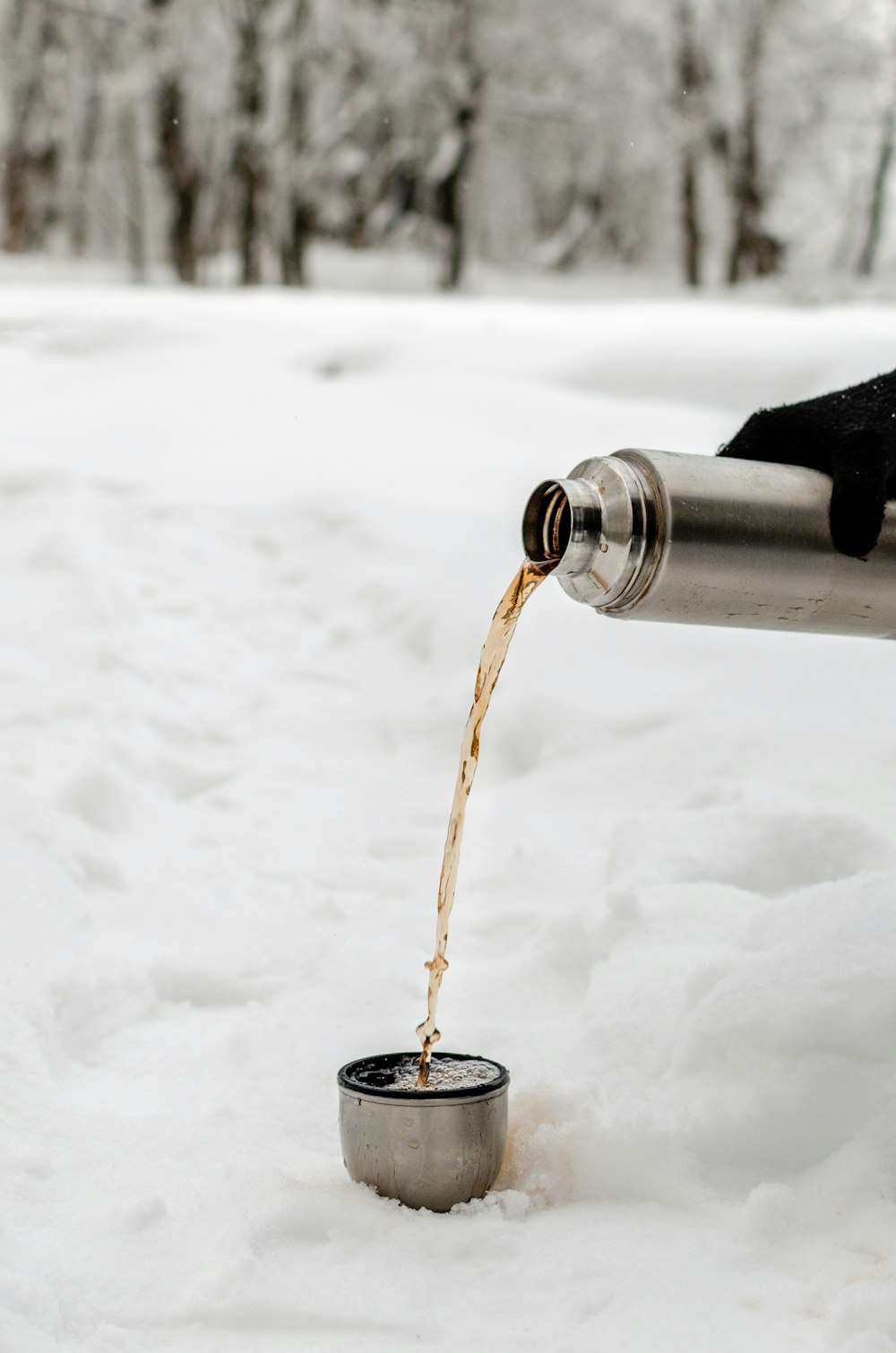 Person gießt Isolierflaschenabdeckung auf weißen, schneebedeckten Boden