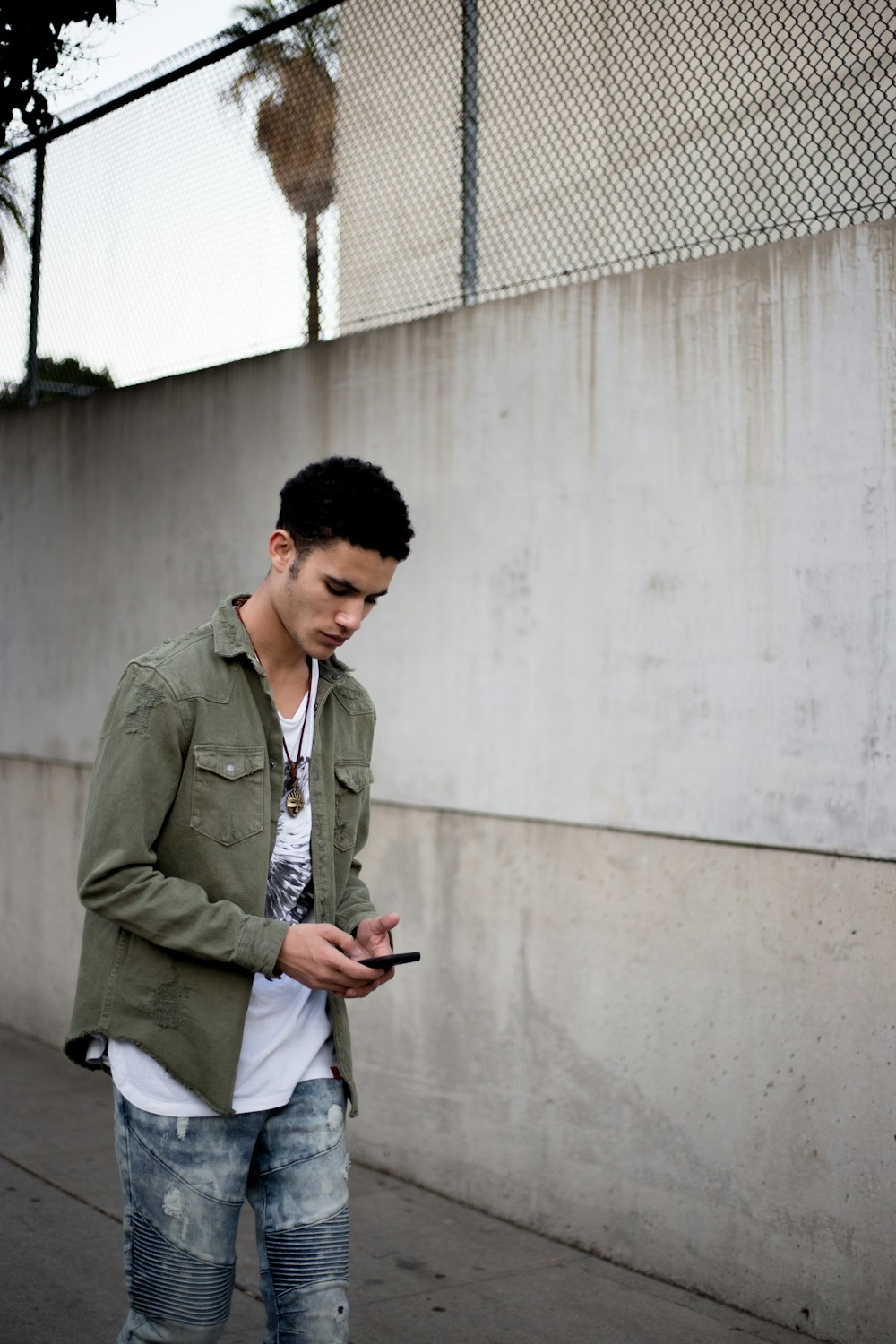 man looking down while holding phone near wall