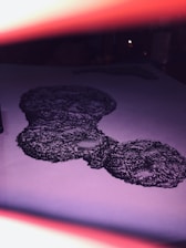 A detailed black ink drawing on white paper, featuring intricate and abstract patterns resembling clusters. The image is partially obscured by a pinkish glow from the top and bottom edges that enhances the artistic effect.