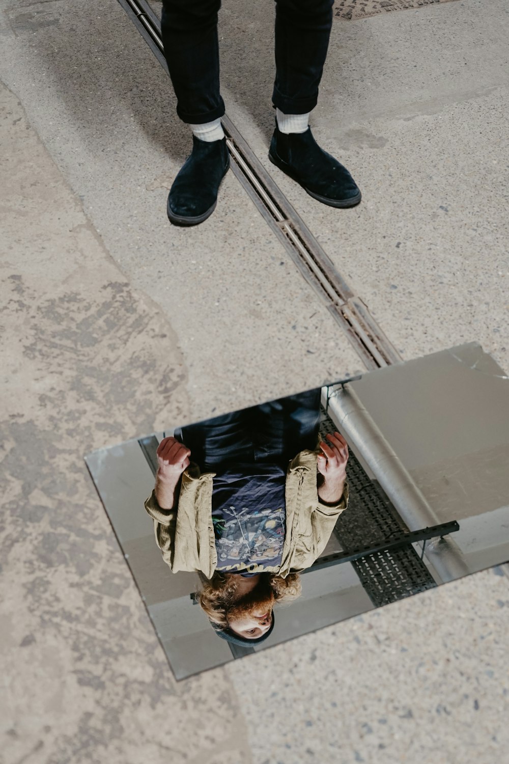 Mujer en chaqueta marrón que se refleja en el espejo en el suelo