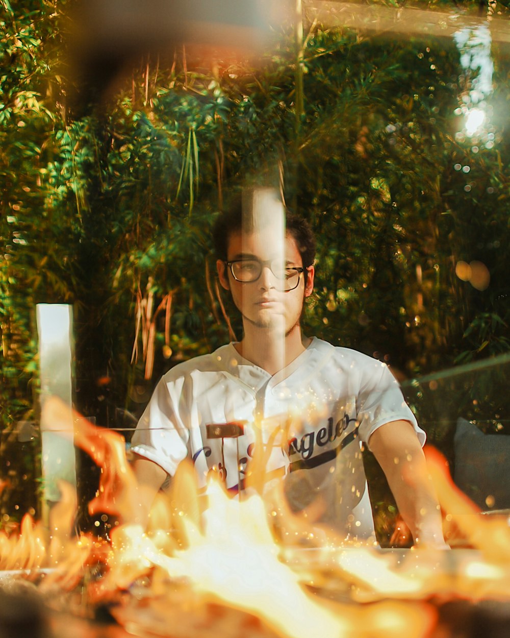 man wearing white and black shirt sitting near green grass with view of flame