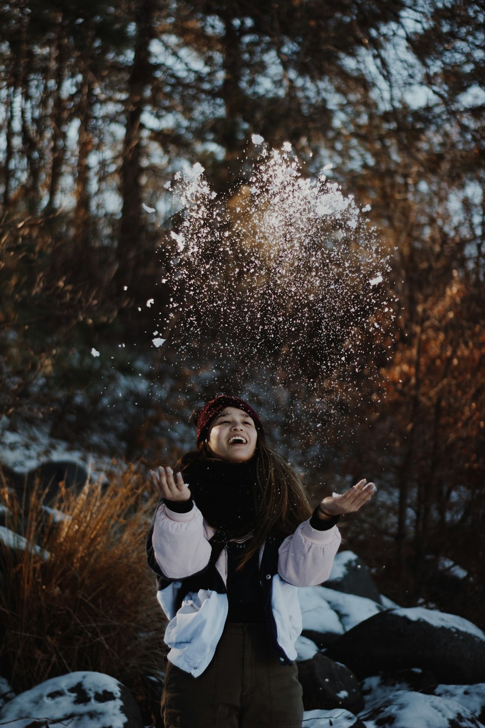 smiling woman throwing snows up in the air near woods during daytime